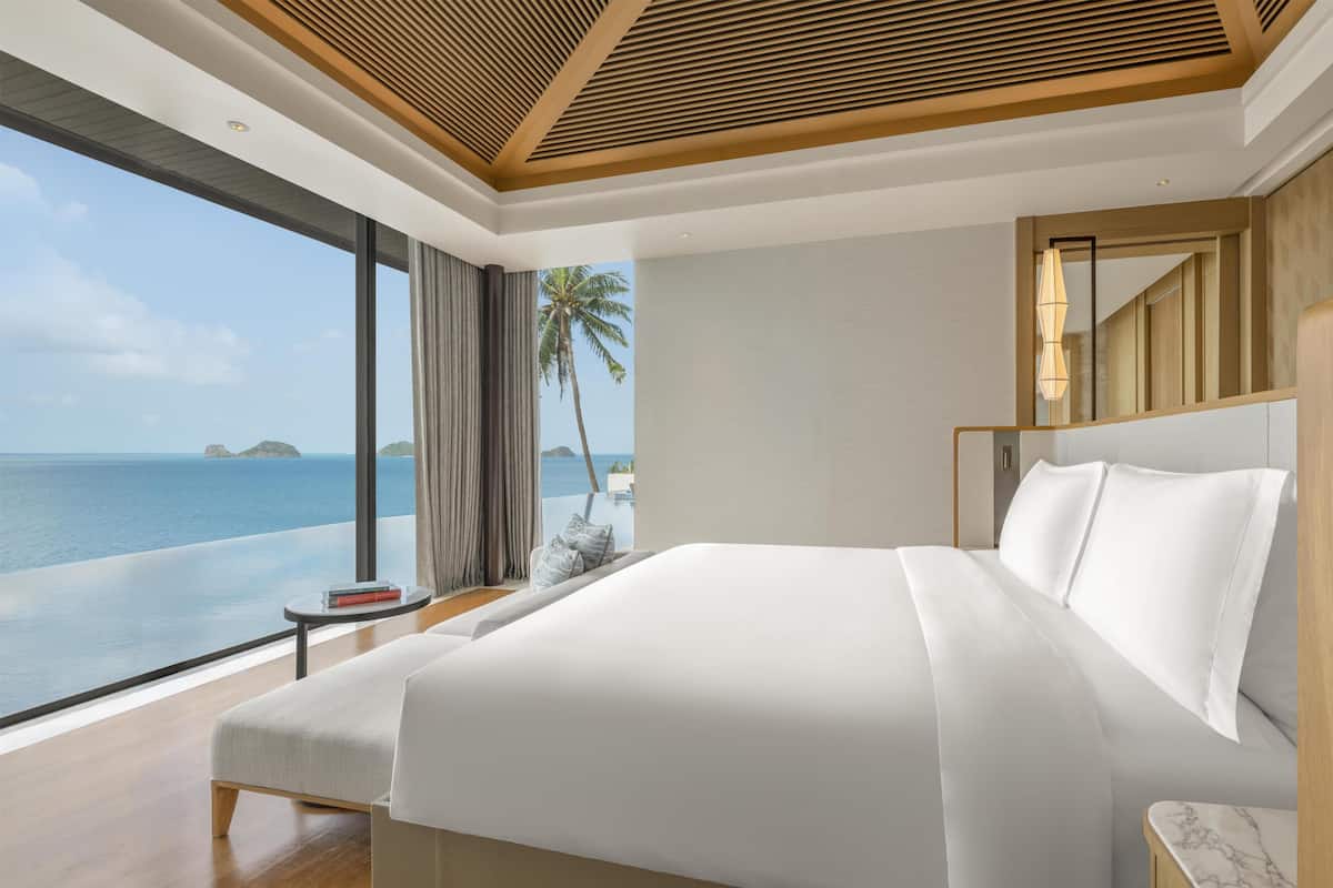 A modern hotel room with a large bed, a small side table, and a view of the ocean.
