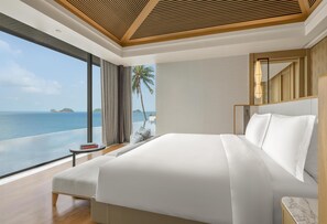 A modern hotel room with a large bed, a small side table, and a view of the ocean.