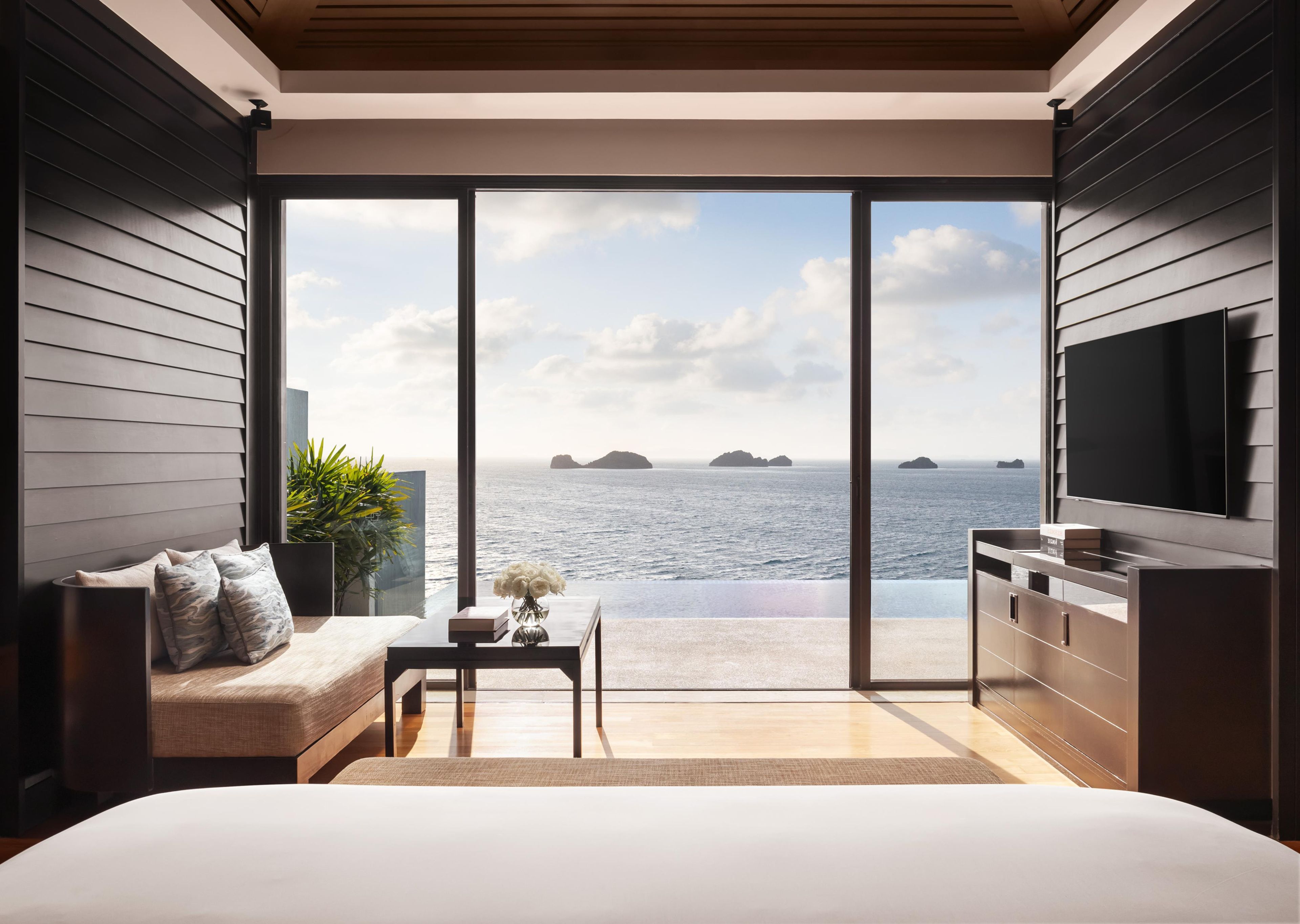 Un dormitorio moderno con un amplio ventanal corredera que da a un balcón con vista al mar.