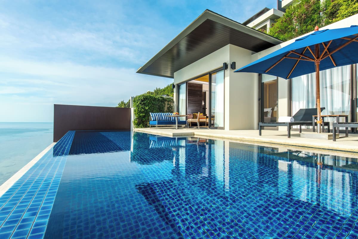 A modern pool area with clear blue water, a covered seating area, and a view of the sea.