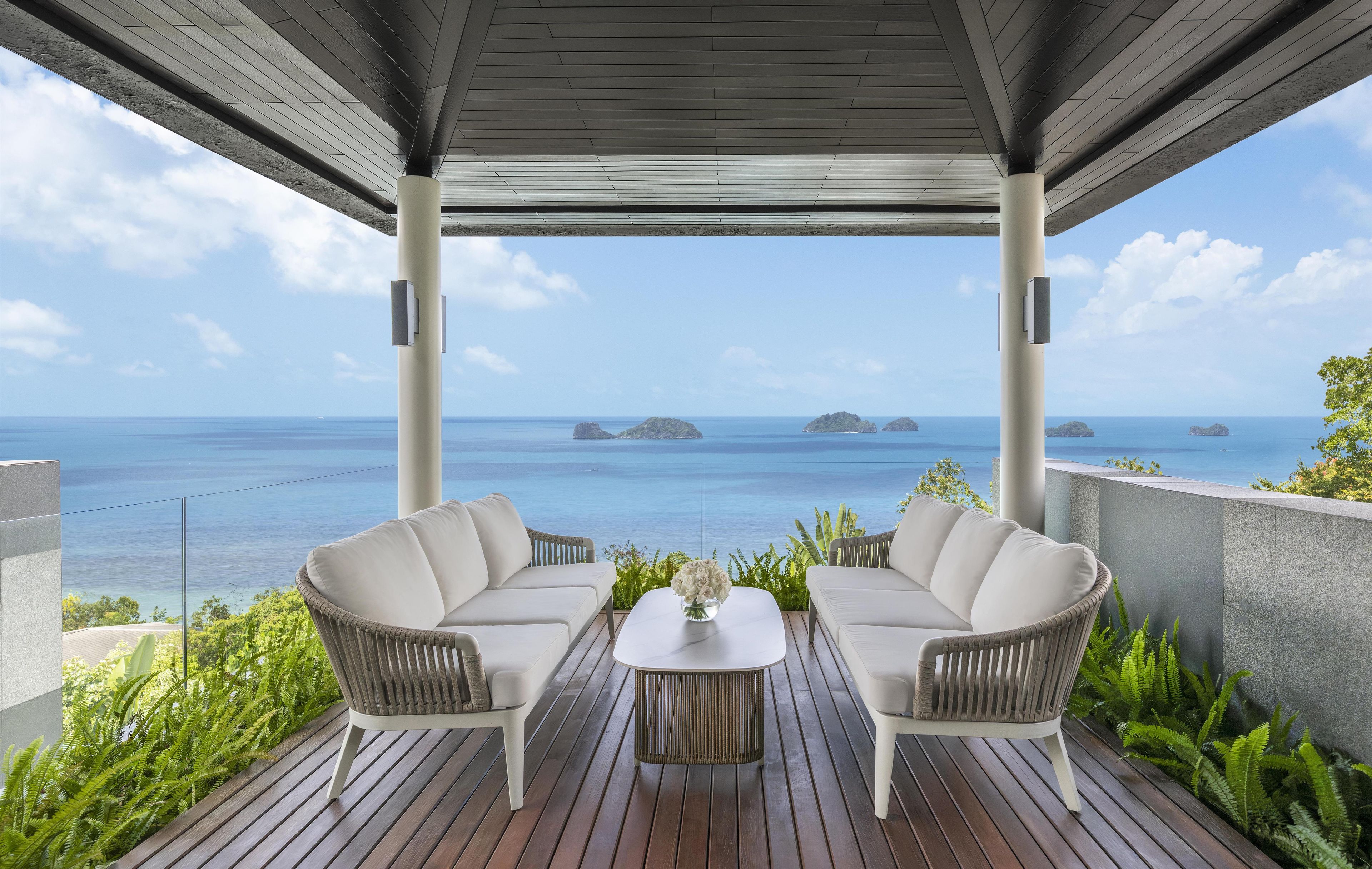A covered outdoor seating area with two sofas and a coffee table, overlooking the sea with islands in the distance.