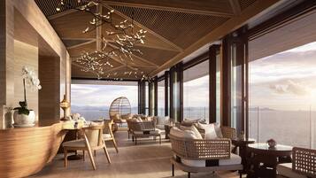 Un intérieur moderne avec un espace salon donnant sur un plan d’eau, agrémenté d’un plafond en bois, de grandes fenêtres et d’une vue sur des montagnes lointaines.