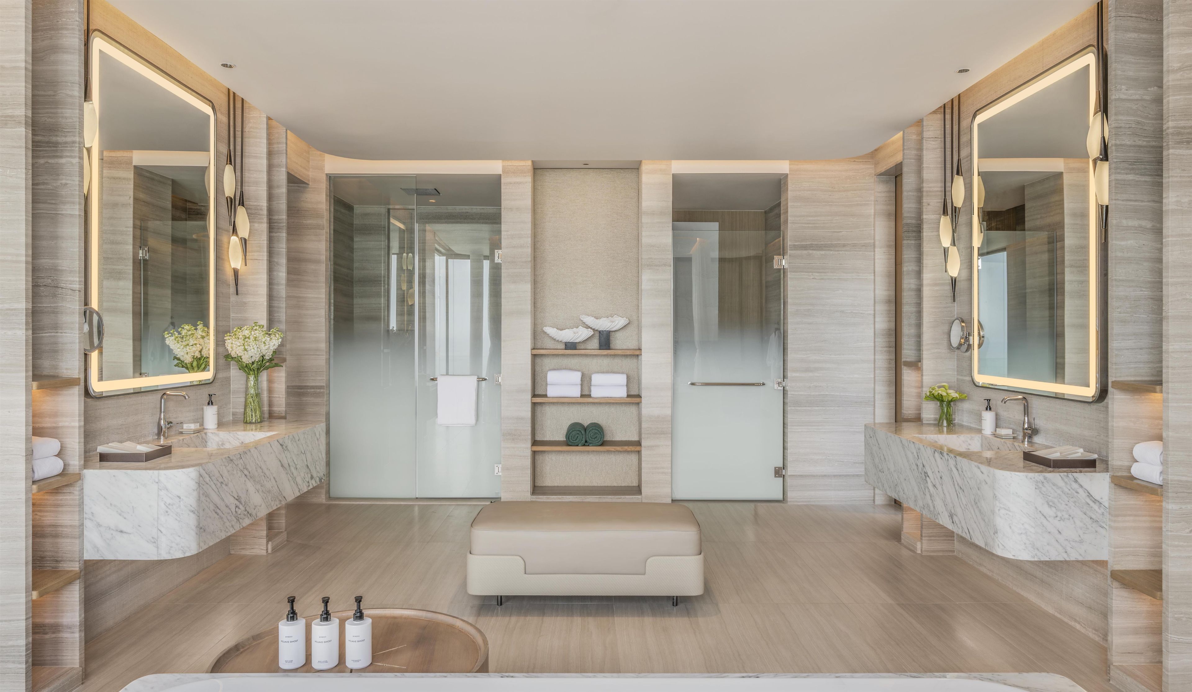 A modern bathroom with two sinks, large mirrors, a bench, and a glass shower enclosure.