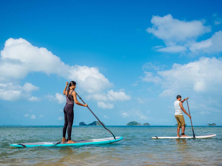 Two people paddleboarding on a calm sea with clear skies and distant islands.