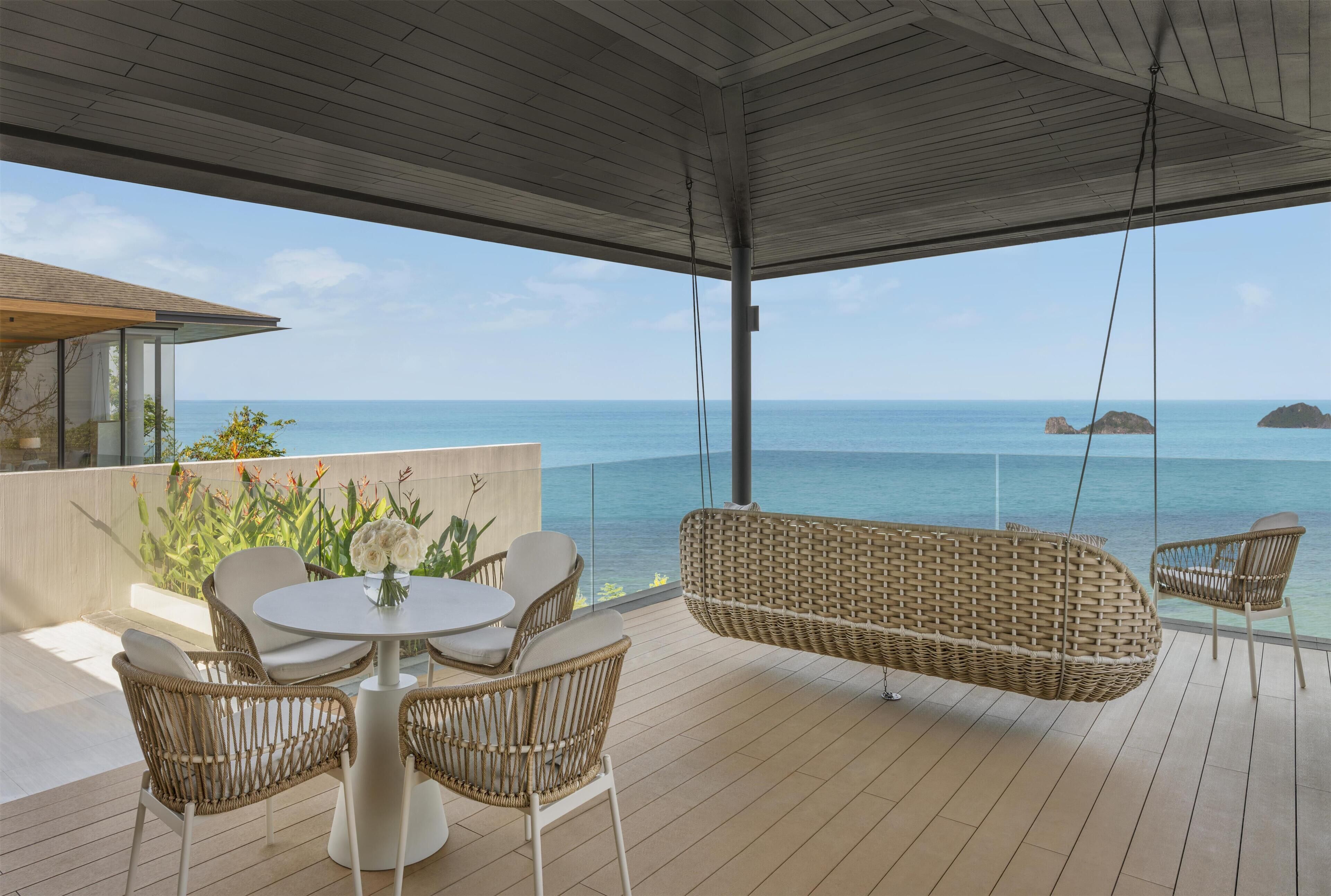 A covered outdoor area with a table and chairs, a hanging chair, and a view of the ocean.