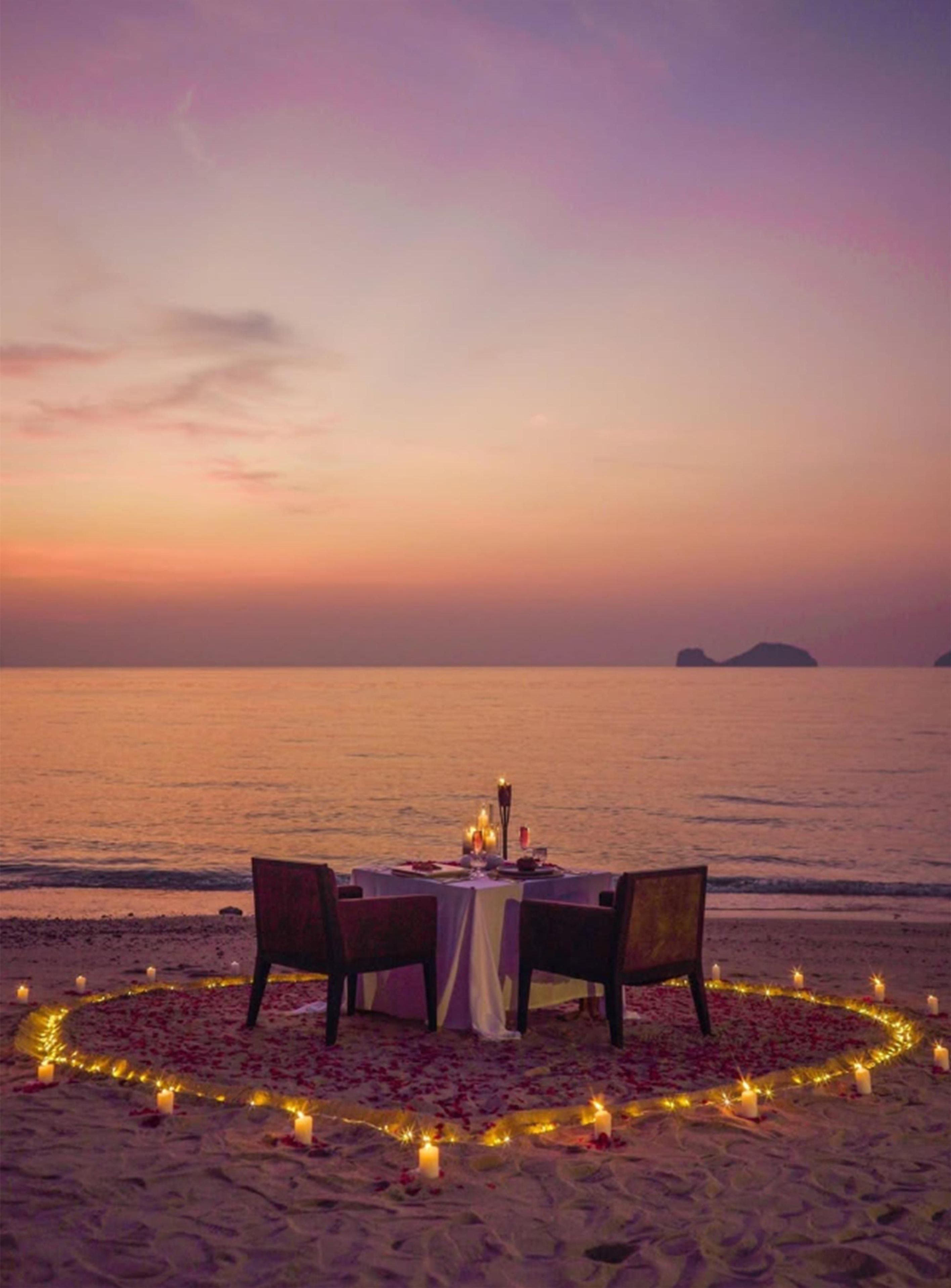 Une table romantique dressée sur la plage, avec des chaises et des bougies.