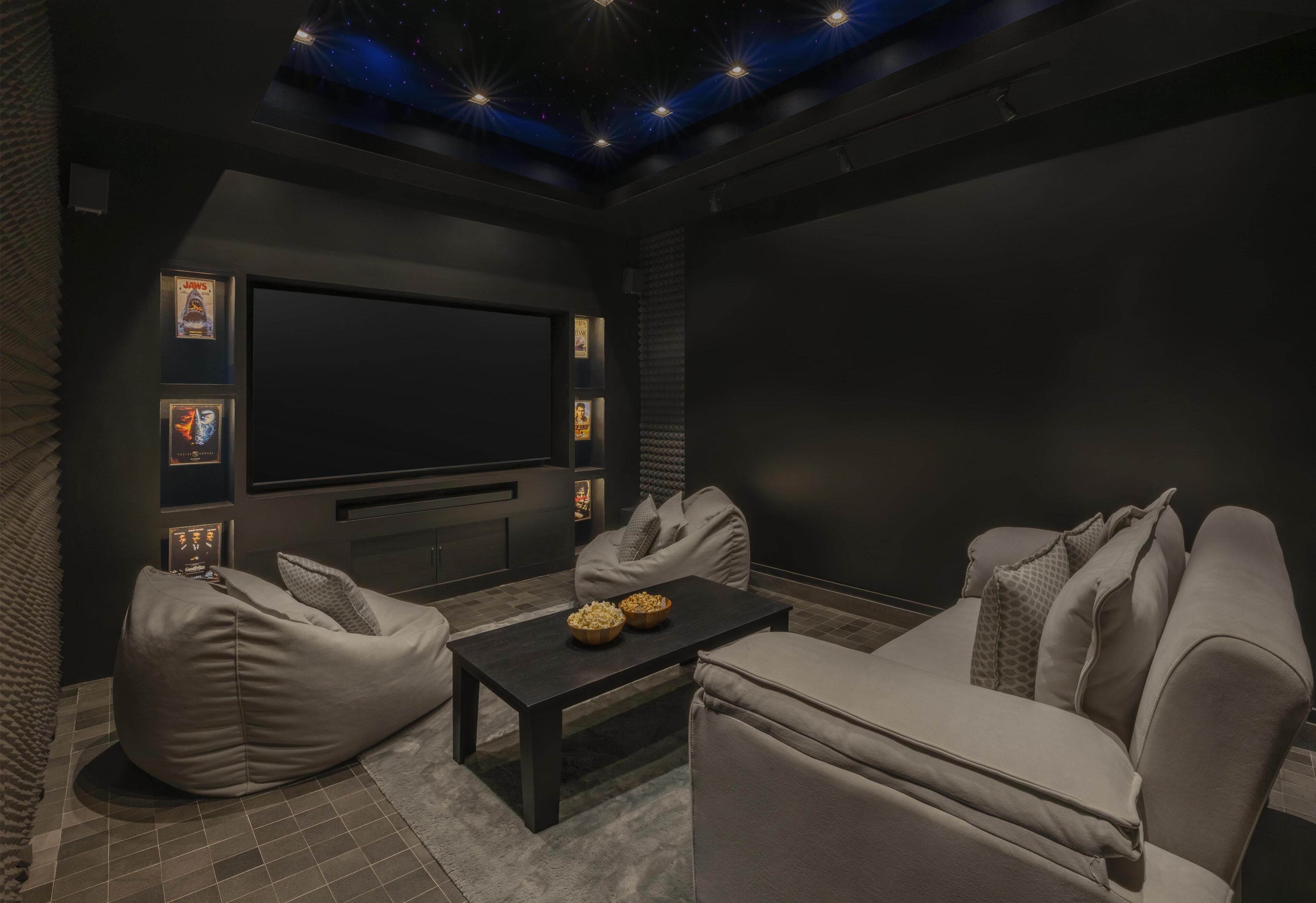 A home theater room with a large screen, bean bag chairs, a coffee table, and framed movie posters.