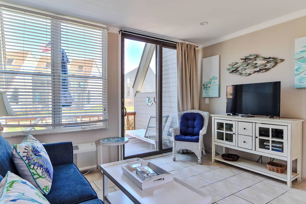 A living room with a sofa, a television, a cabinet, and a sliding glass door leading to an outdoor area.
