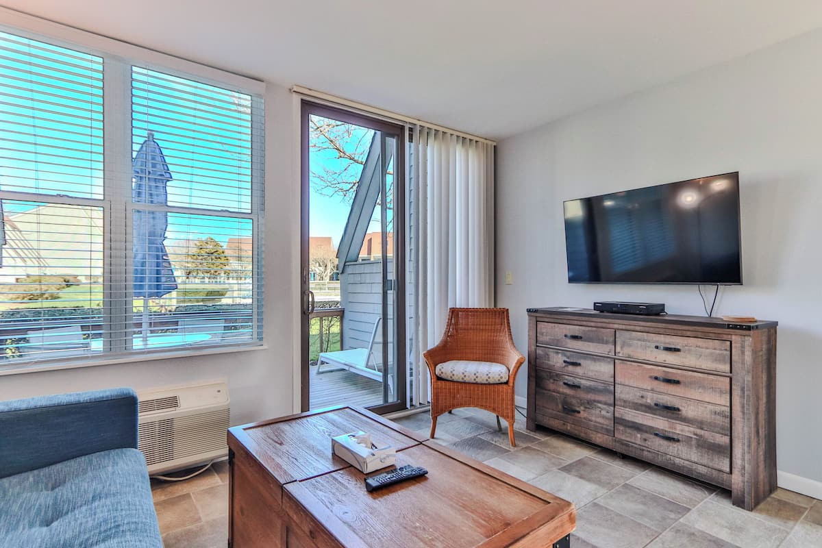 A living room with a TV, a wicker chair, a sofa, a coffee table, and a sliding glass door leading to an outdoor area.