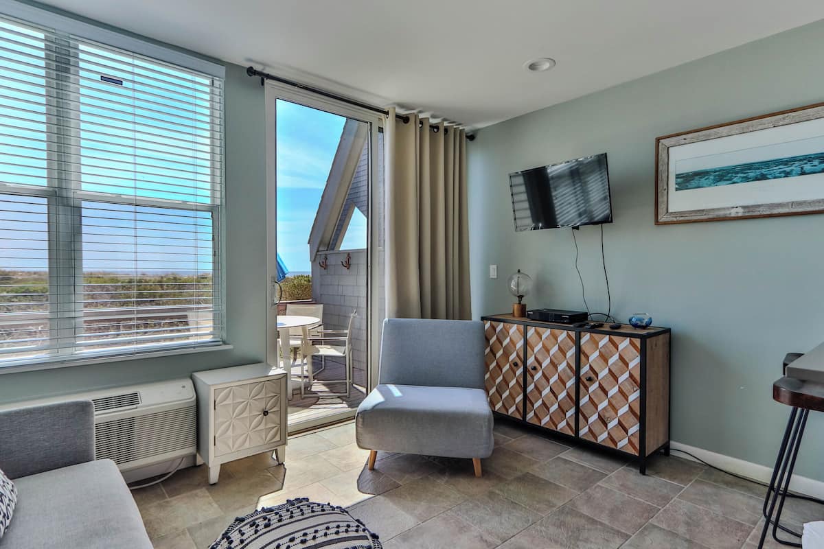 A room with a sofa, a chair, a TV, a cabinet, and a view through a door.