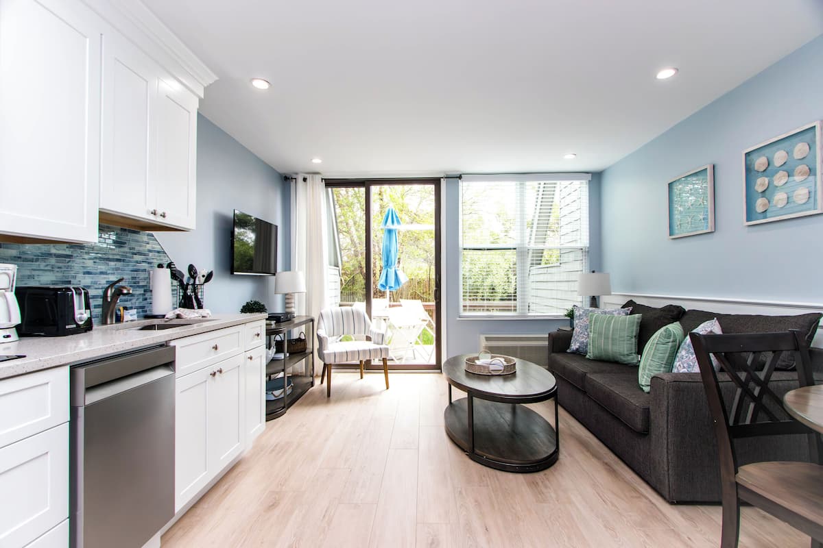 A modern kitchen with white cabinets, a dishwasher, and a dining area with a dark sofa and a round table.