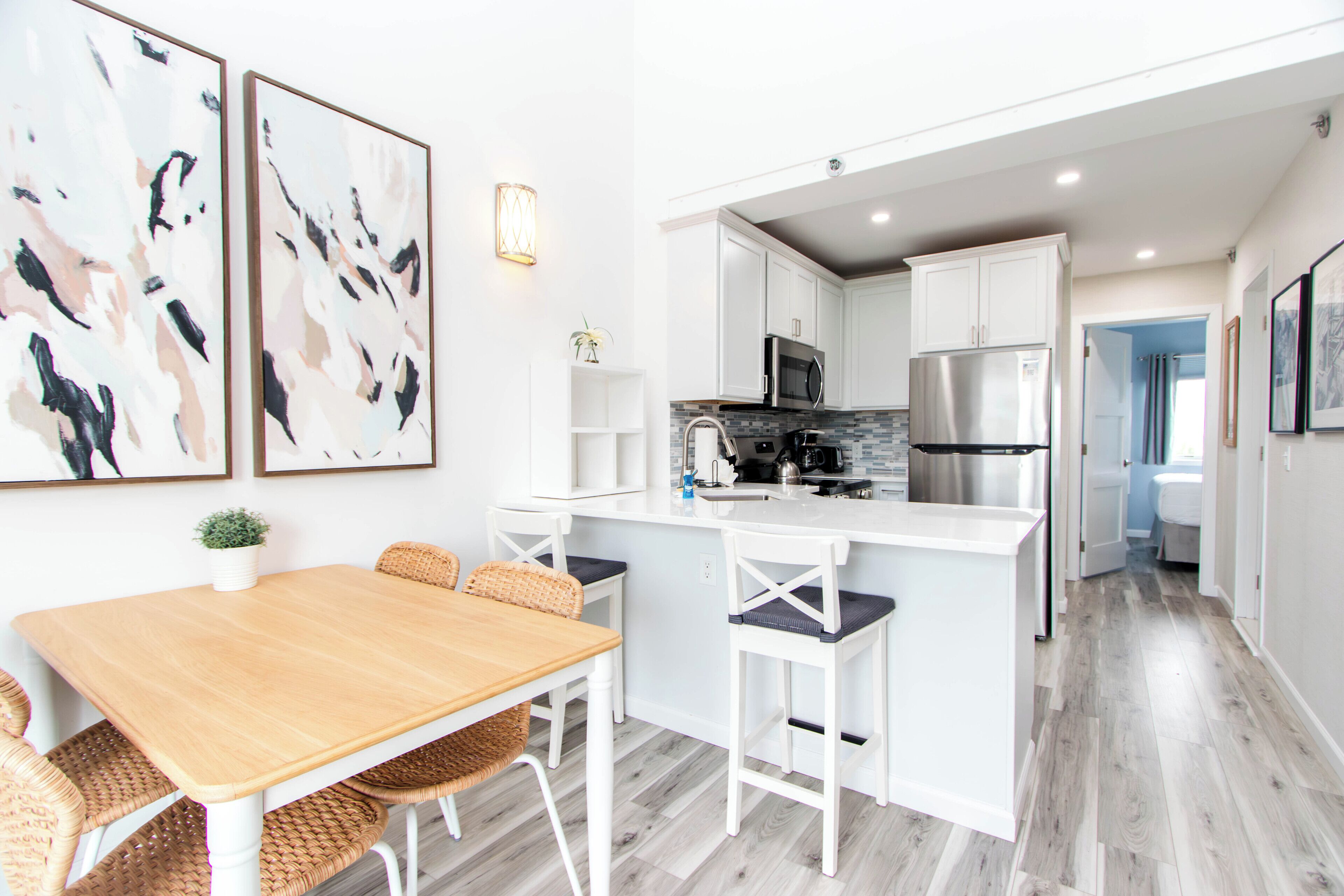 A modern kitchen with white cabinetry, a central island, and a dining area with wicker chairs.
