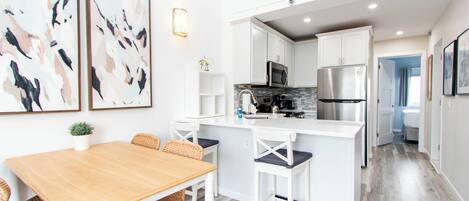 A modern kitchen with white cabinetry, a central island, and a dining area with wicker chairs.