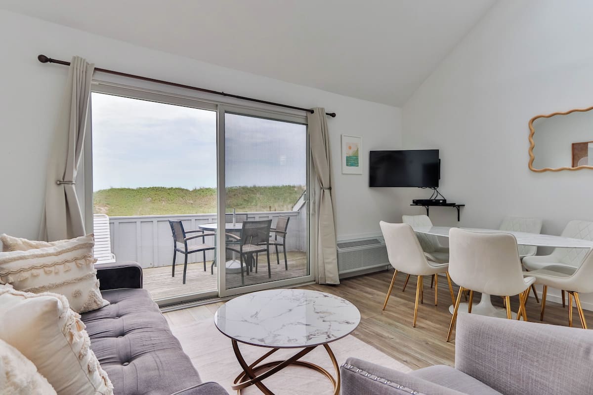 A modern living room with a sofa, a round table, a TV, and a balcony with a table and chairs.