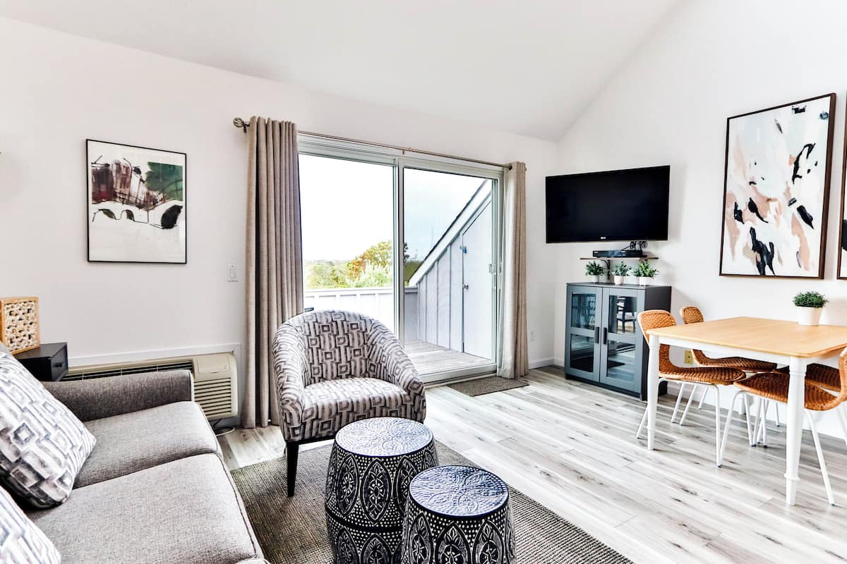 A modern living room with a sofa, armchair, coffee table, dining table, and TV.