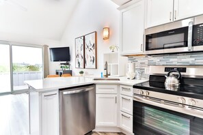 A modern kitchen with white cabinetry, a built-in dishwasher, a stainless steel microwave, and an oven. - Windward Shores Ocean Resort (Amagansett)