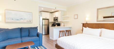 Une chambre d’hôtel moderne avec un canapé, un lit, un coin cuisine et une vue sur l’océan.