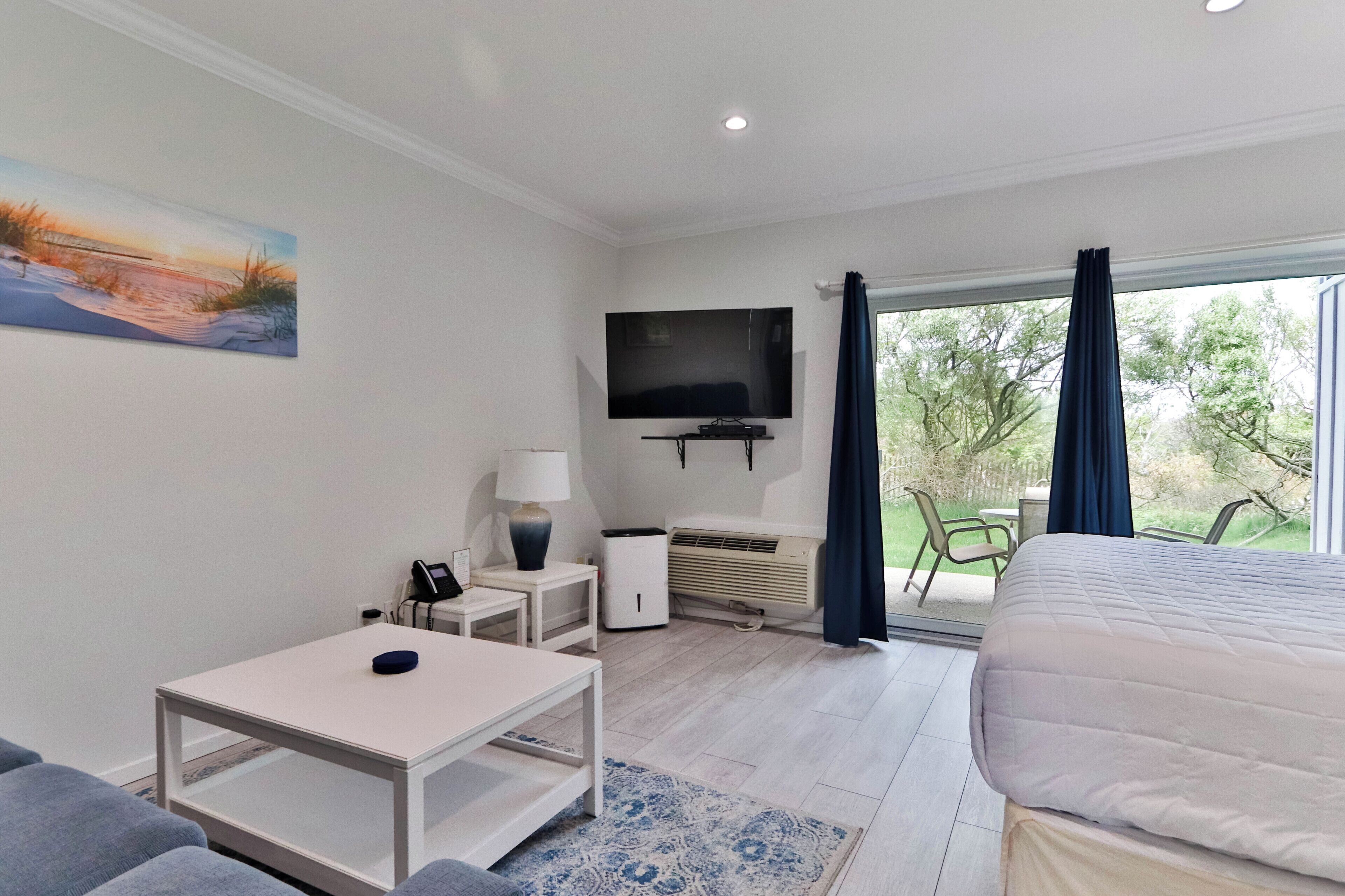 Una habitación de hotel con cama, televisión, escritorio, silla, lámpara y ventana con cortinas.