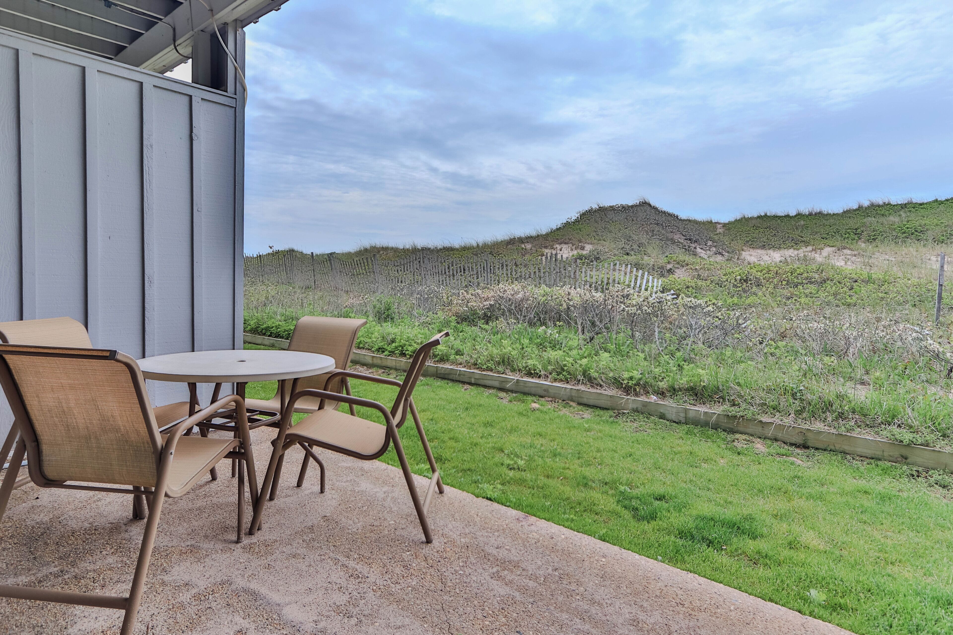 Eine Terrasse mit Tisch und Stühlen, Blick auf einen grasbewachsenen Hügel und einen Holzzaun.