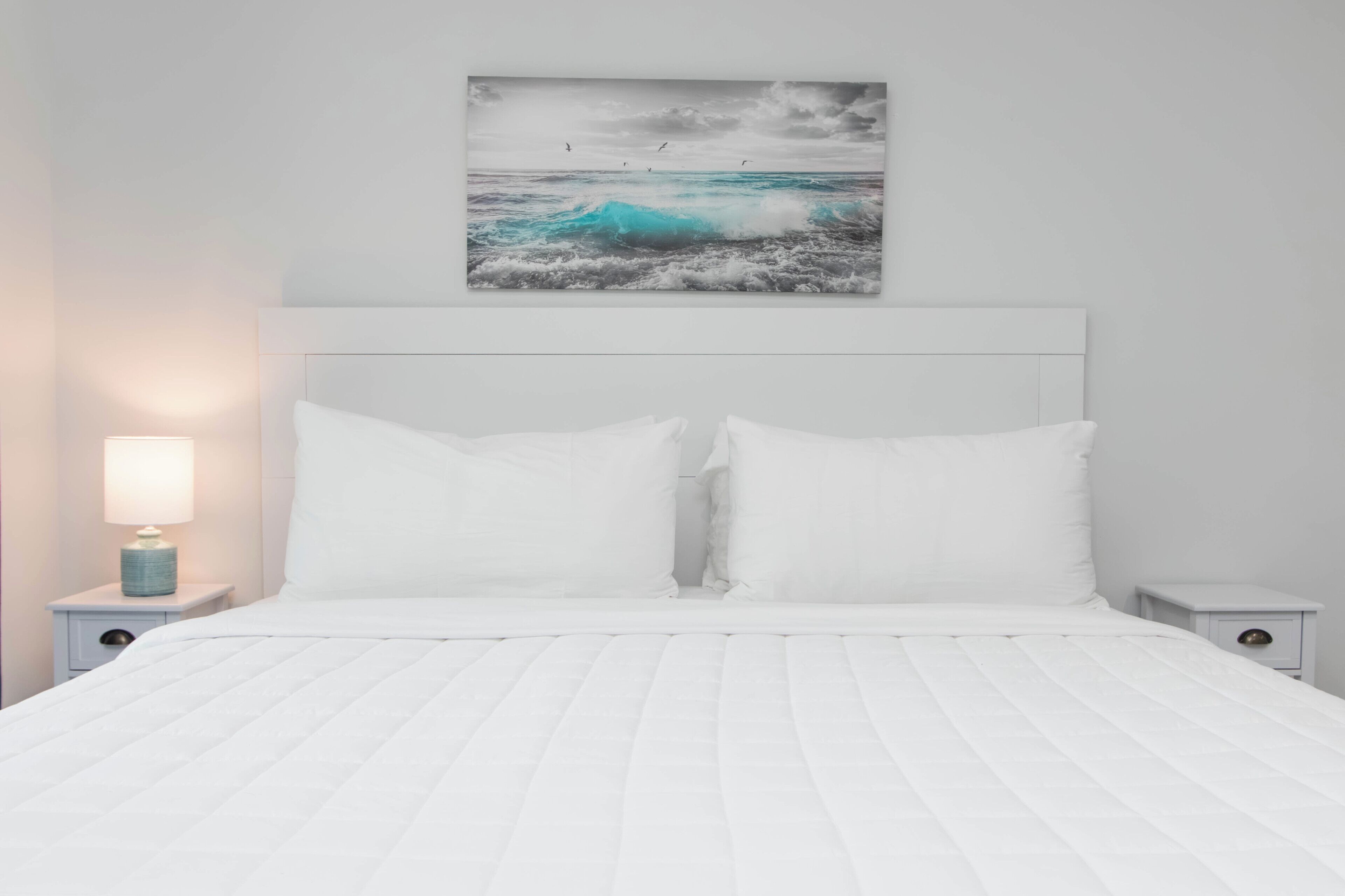 A bed with white bedding, a headboard, and a wall-mounted picture of a wave.