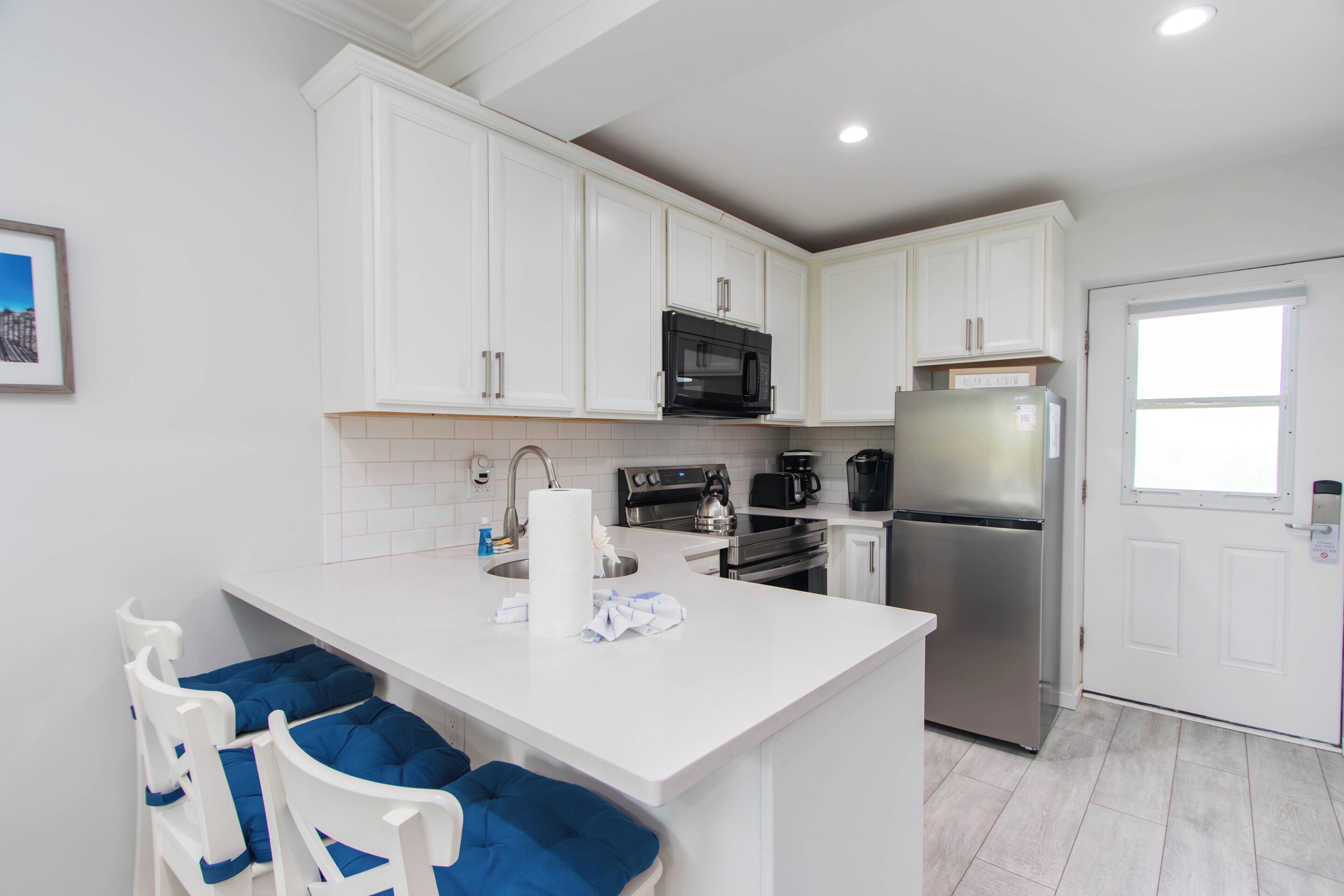 A kitchen with white cabinets, a stainless steel refrigerator, a microwave, and a coffee maker.
