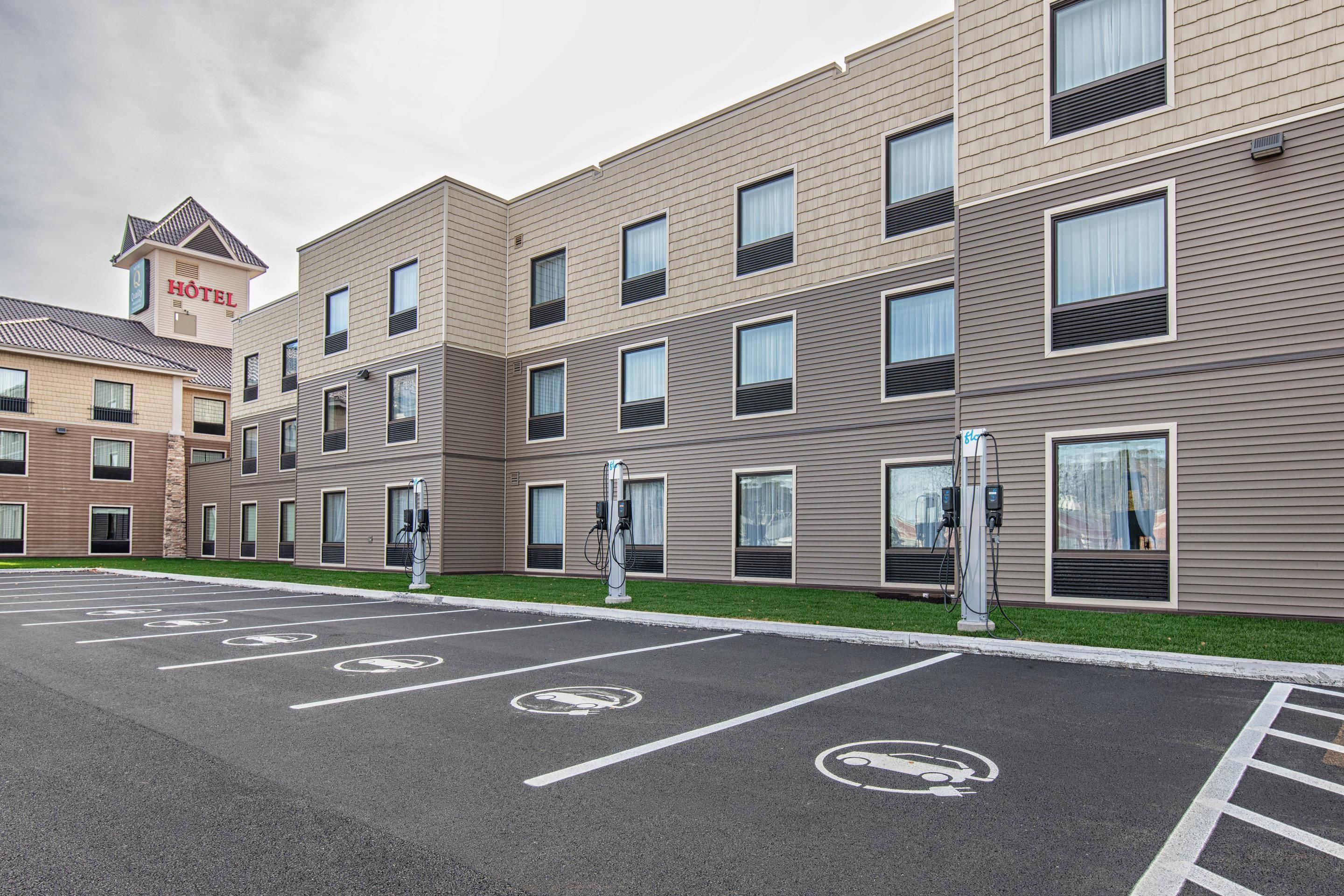 Un moderno edificio de hotel con varios pisos, espacios de estacionamiento señalizados para vehículos eléctricos y un letrero de hotel visible.