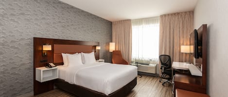 A hotel room with a large bed, a desk, a chair, a TV, and a window with curtains.