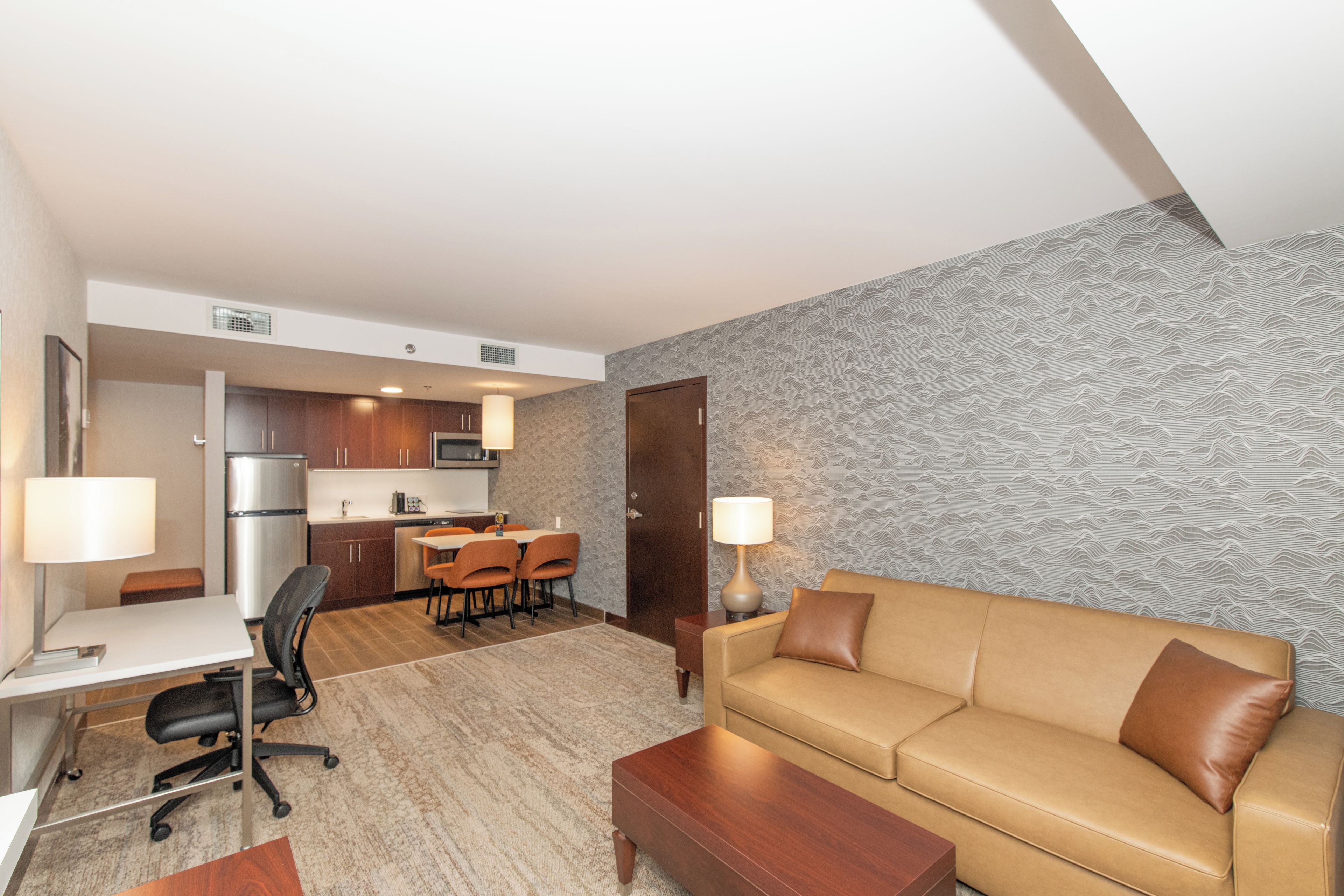 Una habitación de hotel moderna con kitchenette, un sofá, un escritorio y una pared con diseño.