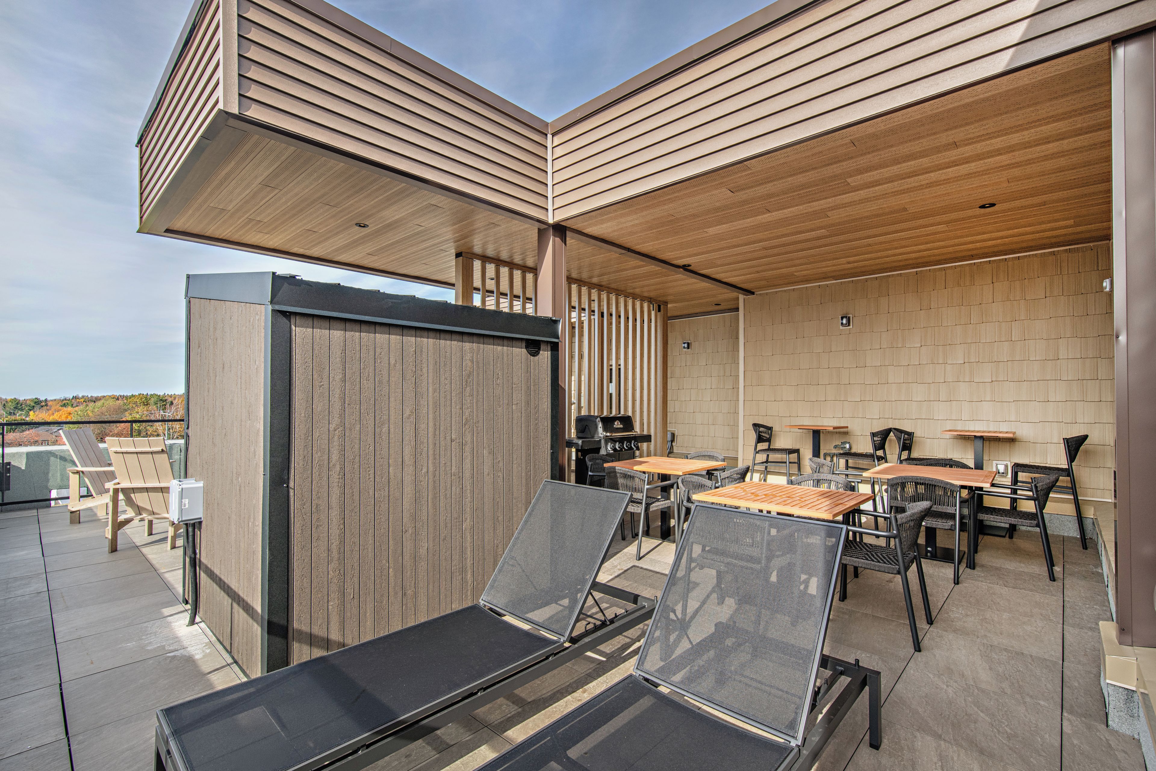 Un espacio de patio al aire libre con muebles de madera, incluyendo mesas y sillas, y una parrilla.