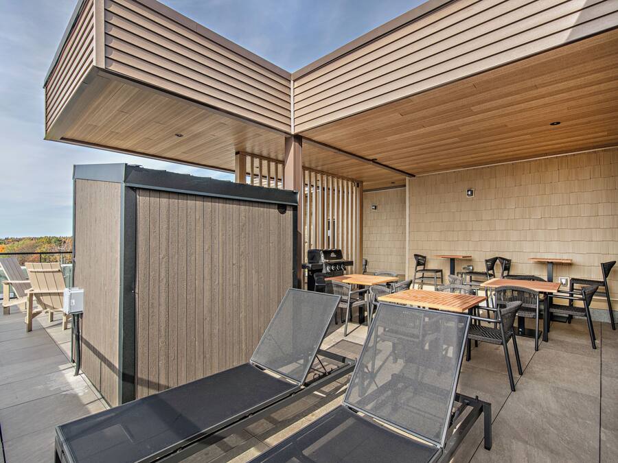 An outdoor patio area with wooden furniture, including tables and chairs, and a grill.