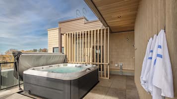 A modern outdoor hot tub area with a wooden deck, a covered seating area, and a view of the surrounding landscape.