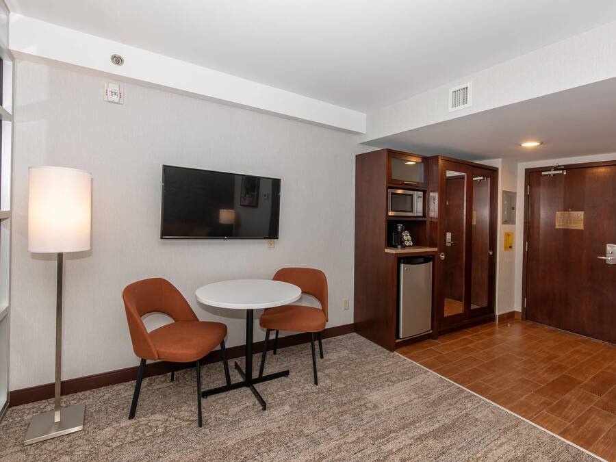 A hotel lobby with a flat-screen TV, a round table with two chairs, a microwave, and a wooden cabinet.
