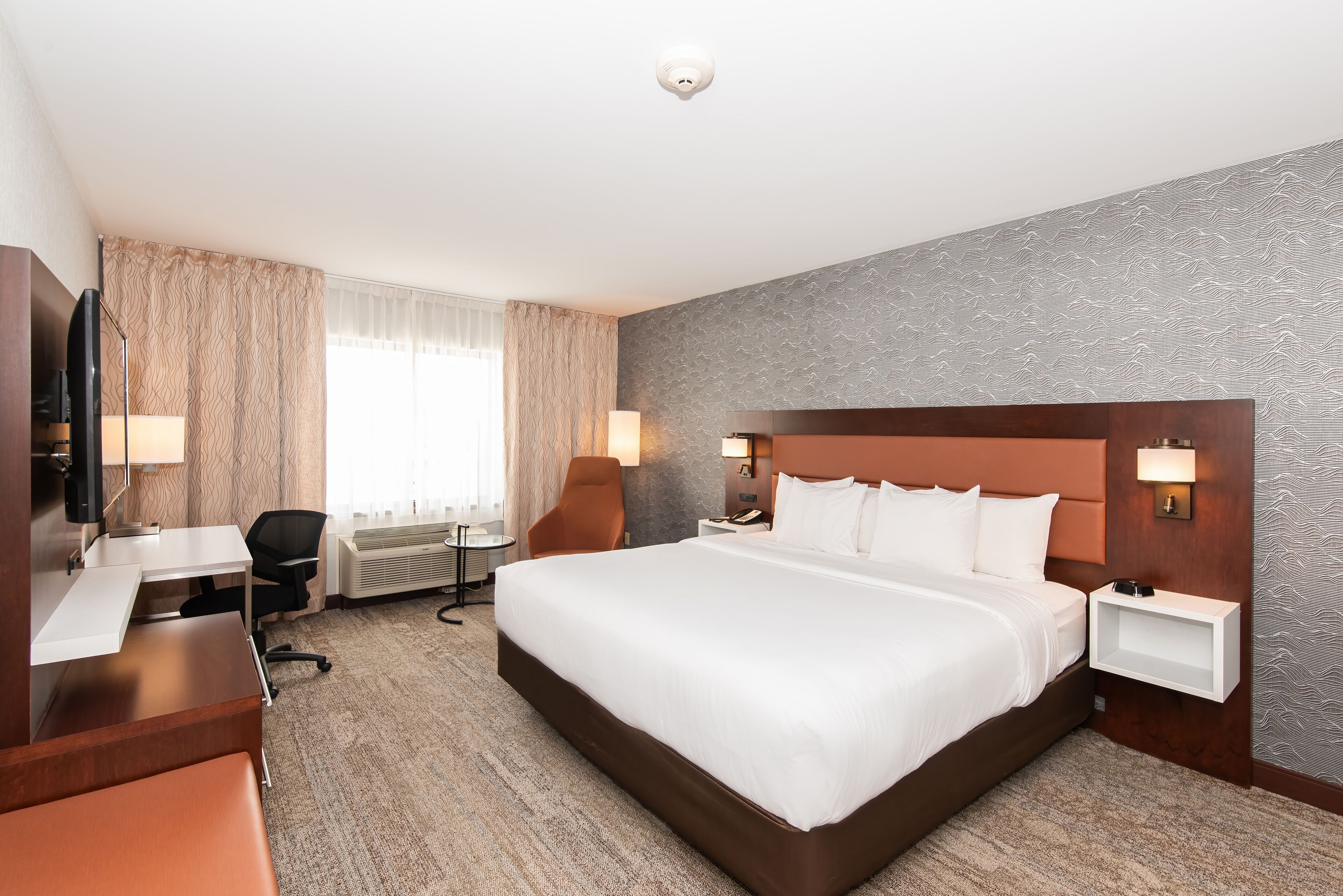 Ein Hotelzimmer mit einem großen Bett, einem Schreibtisch mit Stuhl, einem Fernseher und einer Lampe.