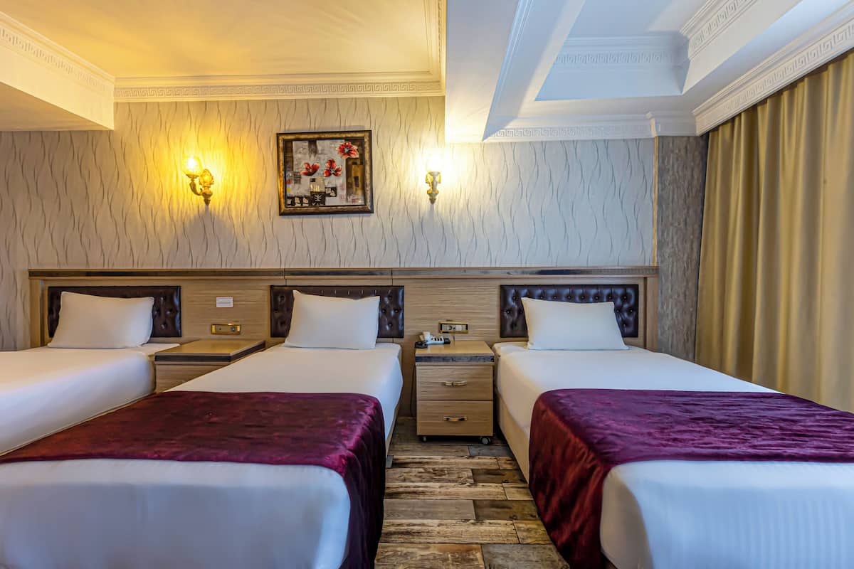 Habitación de hotel con dos camas, cabecero de madera, mesita de noche y una lámpara fijada a la pared.