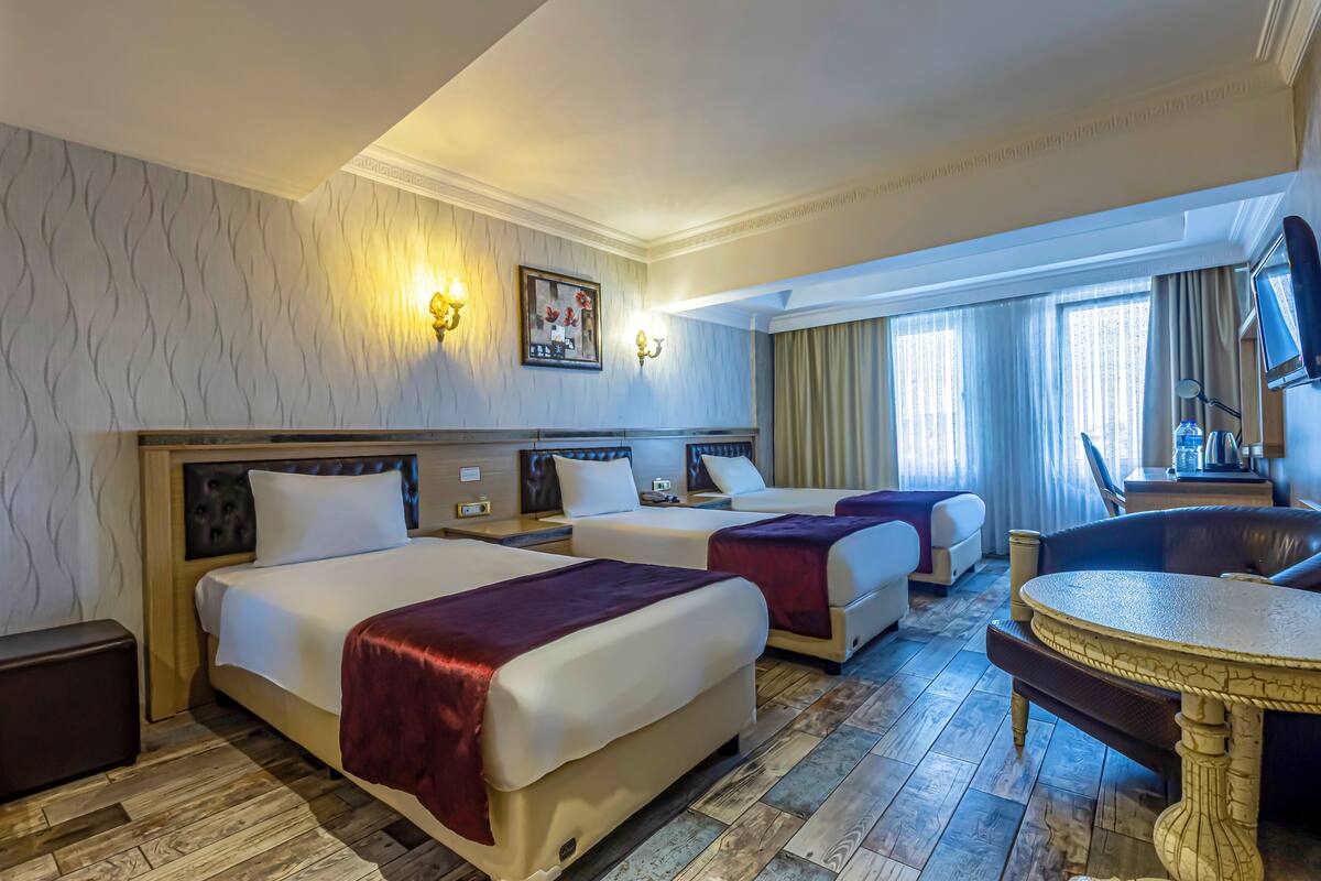 Una habitación de hotel con tres camas, una mesa redonda y una televisión.