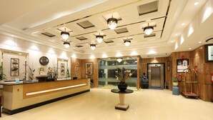 A hotel reception area with a wooden reception desk, a vase with flowers, chandeliers, and an elevator. - Days Hotel by Wyndham Neemrana Jaipur Highway (Neemrana)