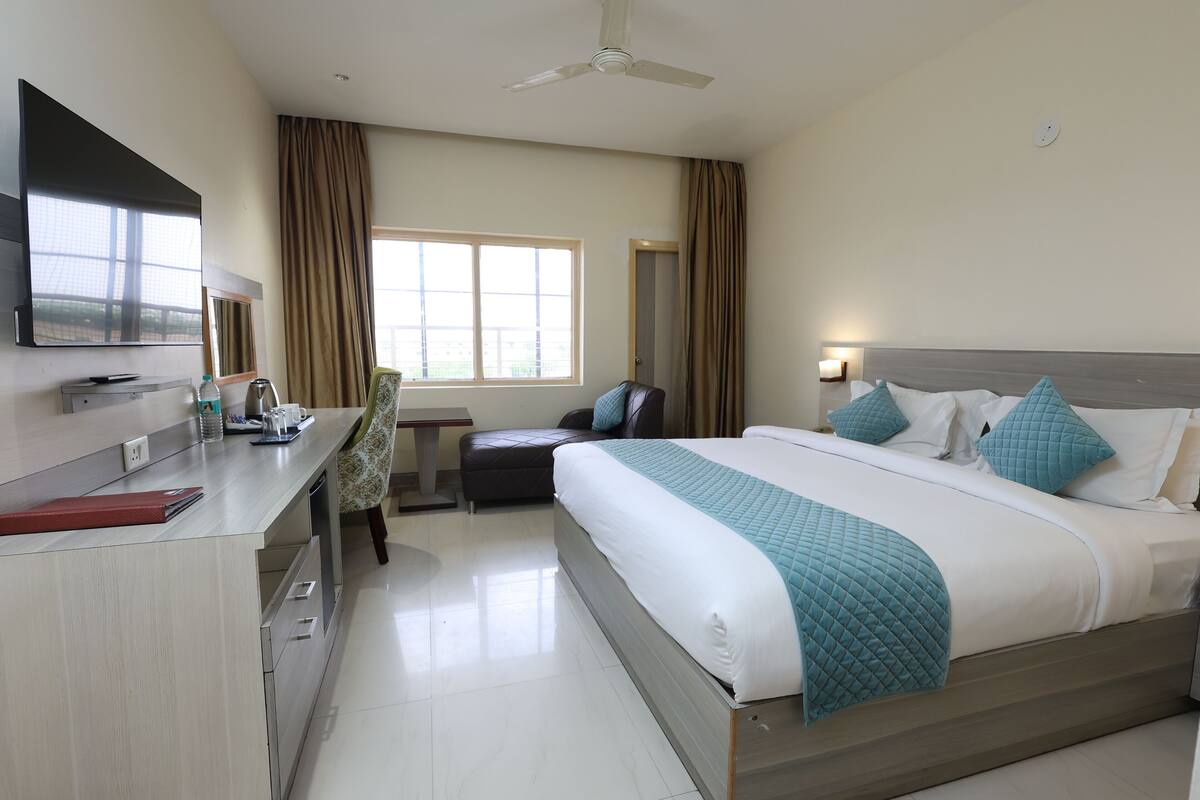 A hotel room with a bed, a desk, a chair, a TV, a window, and a ceiling fan.