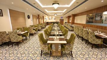 Un comedor de hotel con mesas largas, sillas estampadas en verde y una alfombra con diseño.