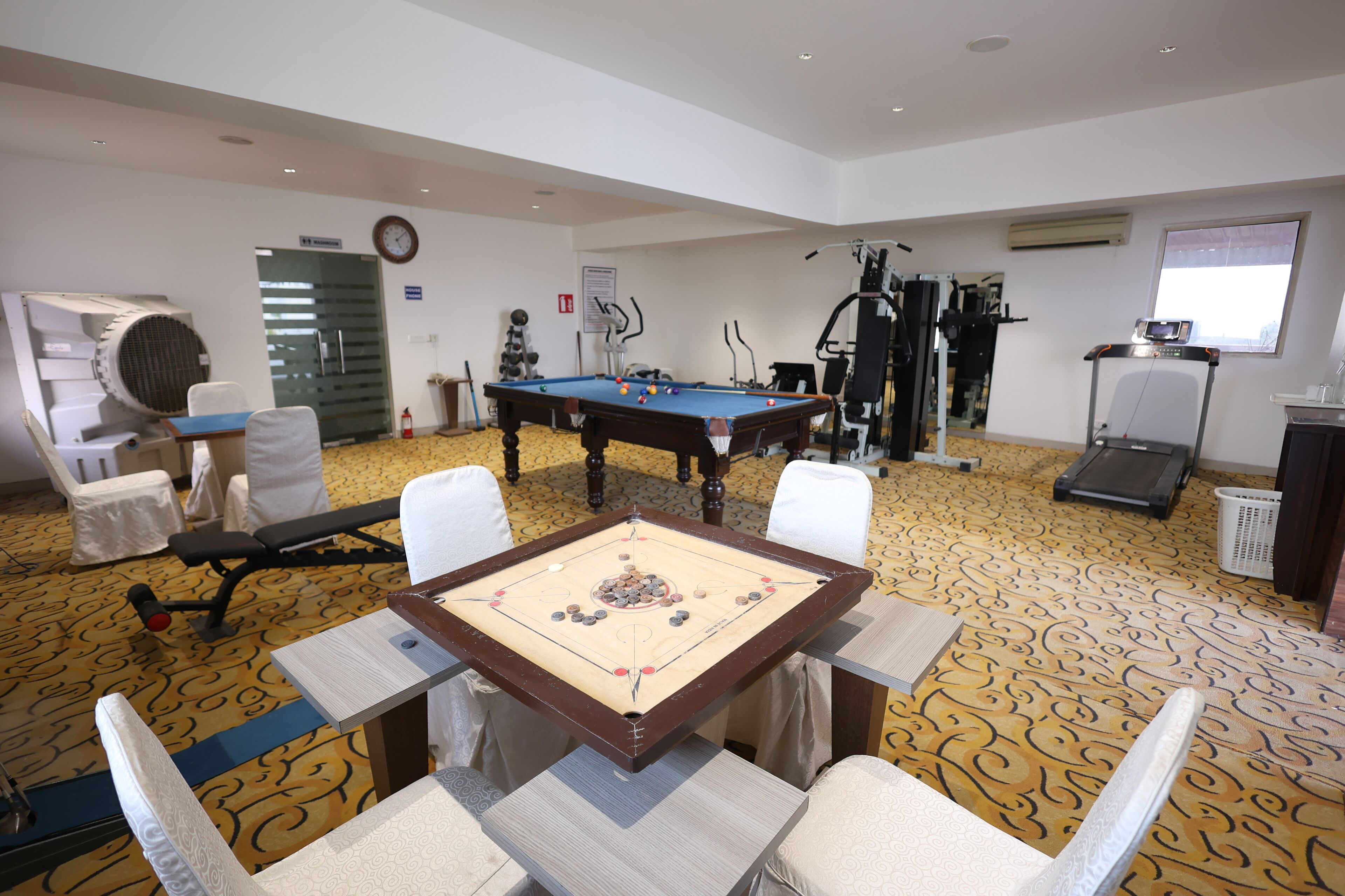 A room with a pool table, exercise equipment, and a clock on the wall.