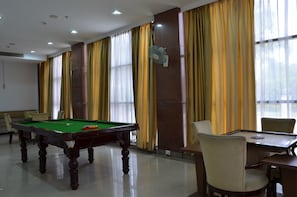 Une table de billard, des chaises, un ventilateur et des rideaux dans une pièce dotée de grandes fenêtres.