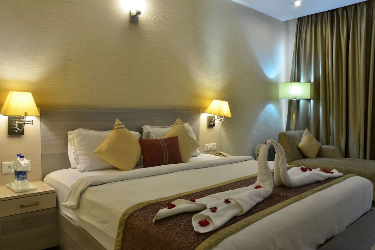 A hotel room with a bed, two bedside lamps, a nightstand, a bottle of water, and a towel with flowers.