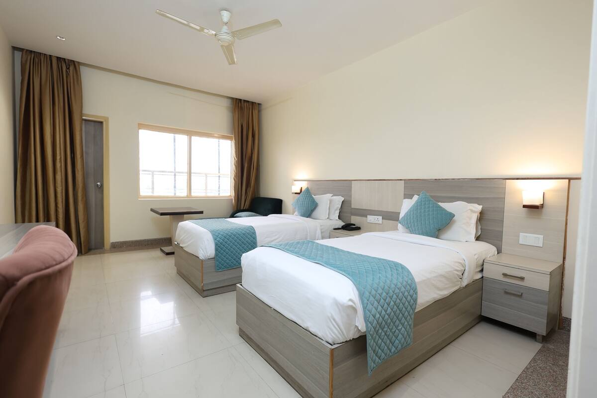 A hotel room with two beds, a desk, a chair, a ceiling fan, and a window with curtains.