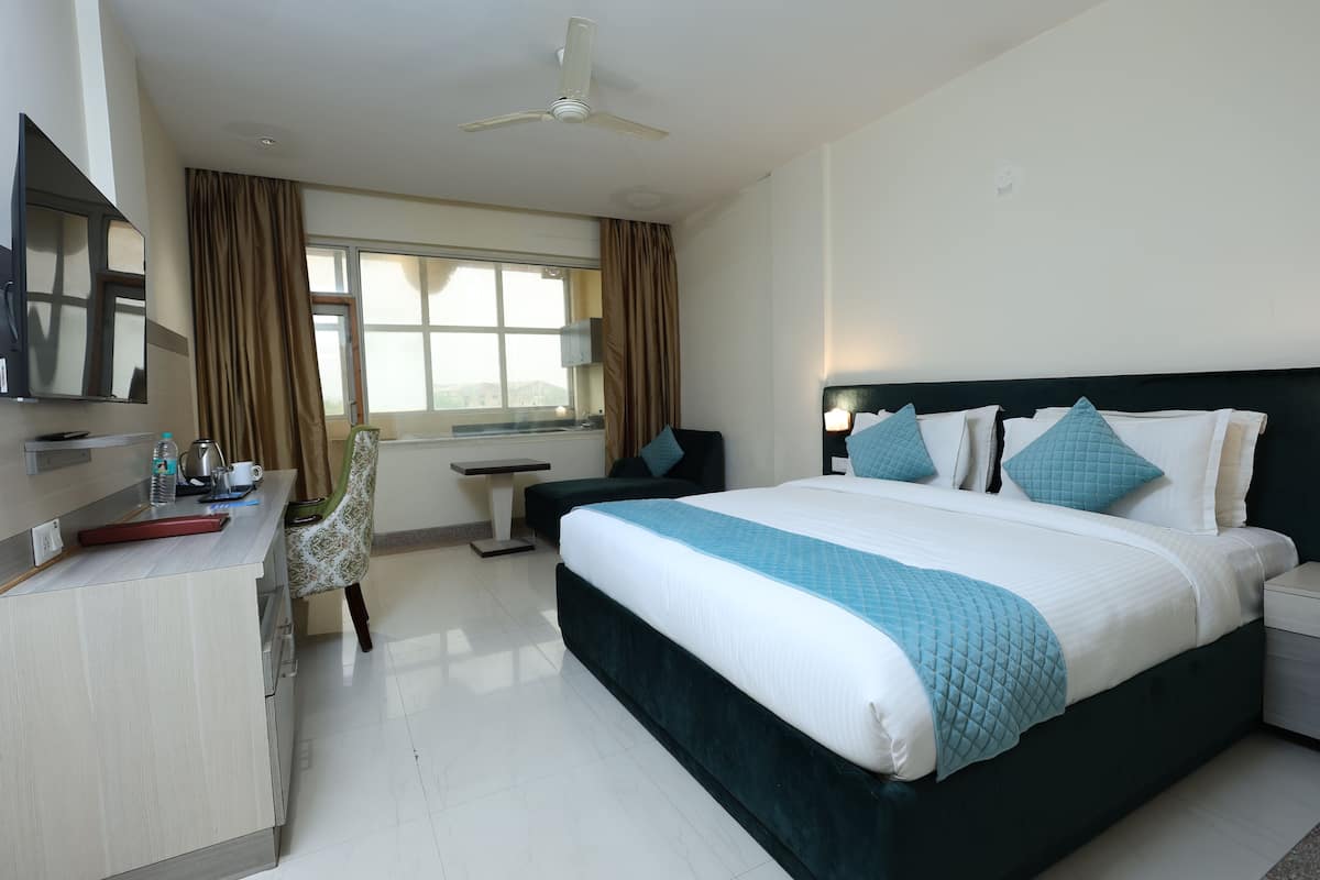 A hotel room with a bed, bedside table, nightstand, TV, desk, chair, and a window with curtains.
