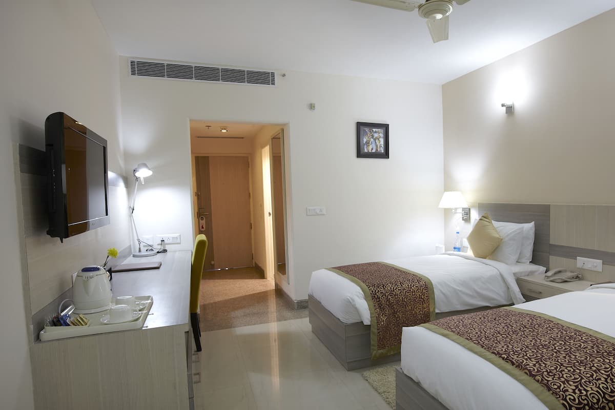A hotel room with two beds, a desk with a lamp, a TV, and a picture on the wall.