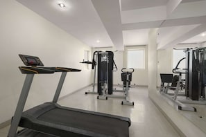 Une salle de sport équipée de tapis de course, d’appareils de musculation et d’un mur entièrement recouvert de miroirs.