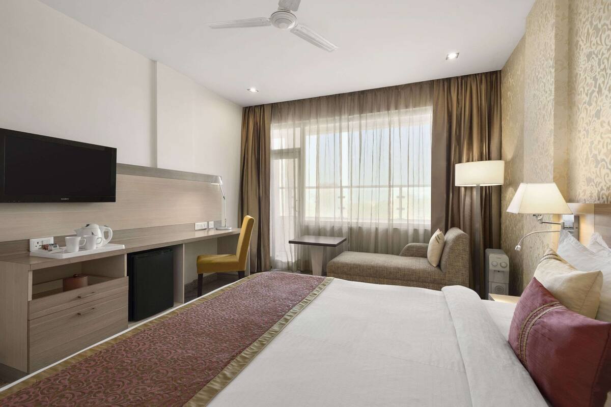 A hotel room with a bed, desk, chair, TV, and a window with curtains.