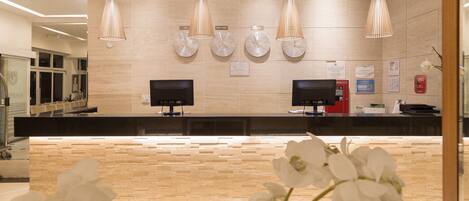 Un área de recepción con un mostrador de madera, dos monitores y tres lámparas colgantes.