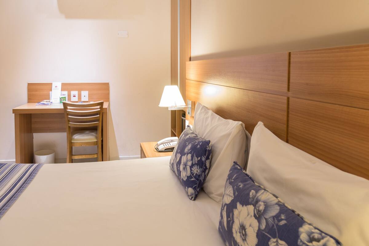 A hotel room with a bed, a desk, a chair, a lamp, and a telephone.