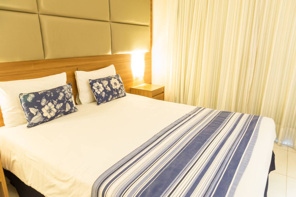 A hotel room with a large bed, two pillows, a nightstand, and a window with curtains.