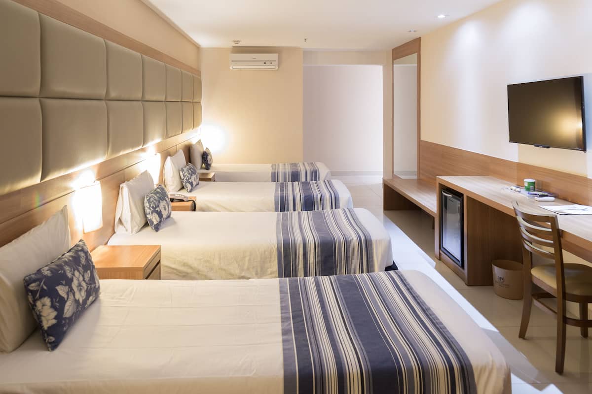 A hotel room with two beds, a desk, a television, and a small kitchenette.